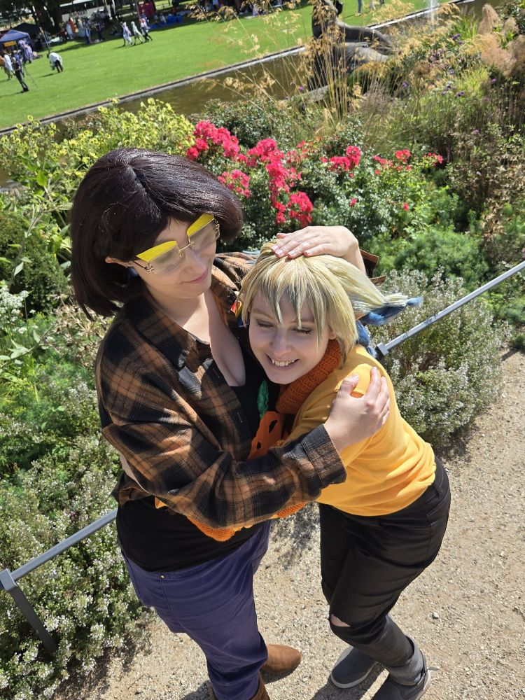 Camila and Vee hugging each other. We are standing on a gravel path in front of some flower bushes.