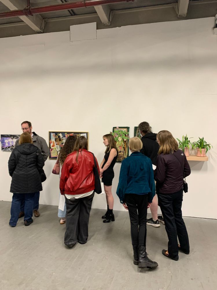 Multiple people standing in front of one of the gallery walls. Parts of four different pieces can be seen behind the group.