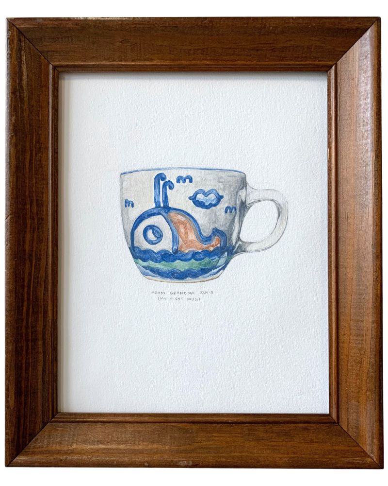 A small, color gouache painting of a mug in a wood frame. The mug has a painted whale on the side, with water below and small clouds surrounding it. The rest of the mug is a pale gray. Below the mug, the following inscription is handwritten in graphite in all capitals: “From Grandma Jan’s (My First Mug)”
