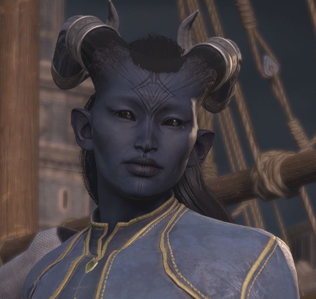 A screenshot of a custom player character from Dragon Age: The Veilguard. The character is a Qunari woman with deep grey skin, black sclera, pointed ears, and long black hair, with silver bands wrapped around two black horns that extend behind her head. She has a diamond-shaped tattoo on her forehead, with two lines from the tattoo that continue down the bridge of her nose and over her lips, ending at her chin. She is wearing a set of dark grey robes with gold trim, and is looking at something off-screen to the right with a mild-mannered expression.