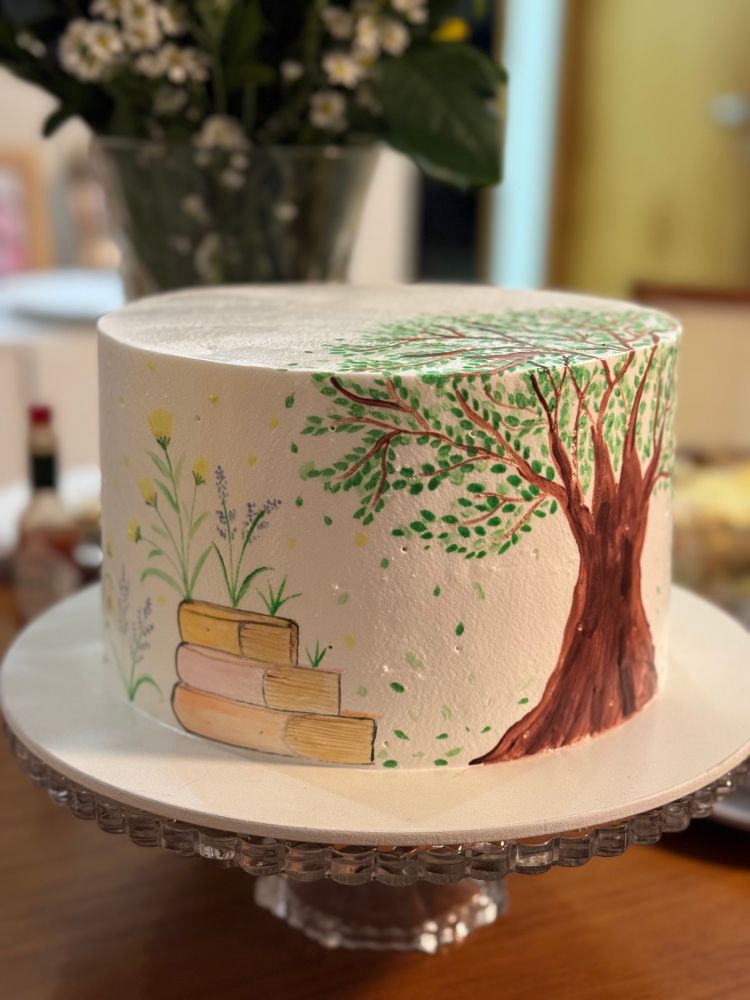 bolo alto decorado com chantilly e pintura de uma árvore e três livros empilhados