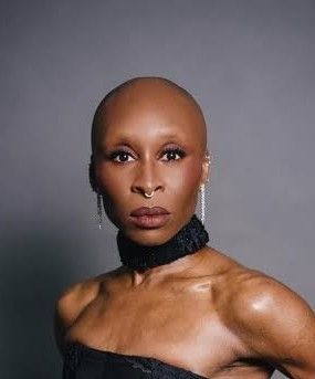 Cynthia Erivo wears a black dress and looks into the camera baldly