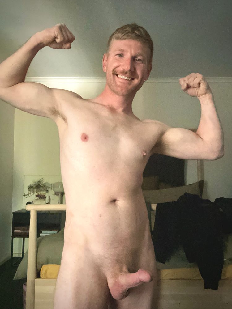 Selfie of a naked man with an erection. He’s smiling and flexing both his arms.