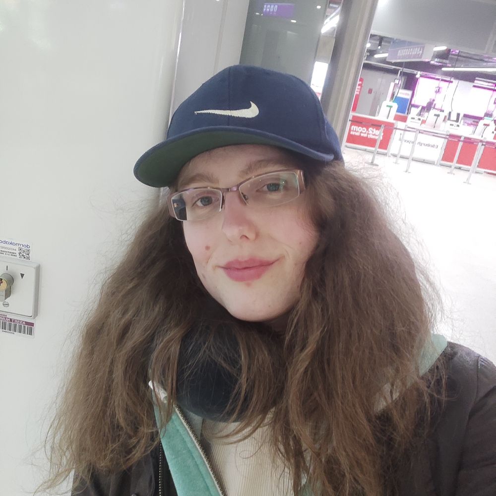 Kris, a woman with long brown hair and rectangular glasses, standing in Edinburgh Airport.