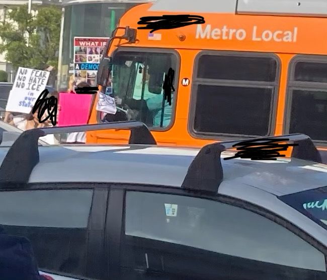 An orange LA metro bus, with a tiny white flag hanging out the driver’s window. If tou look closely, the flag says “Fuck ICE.”