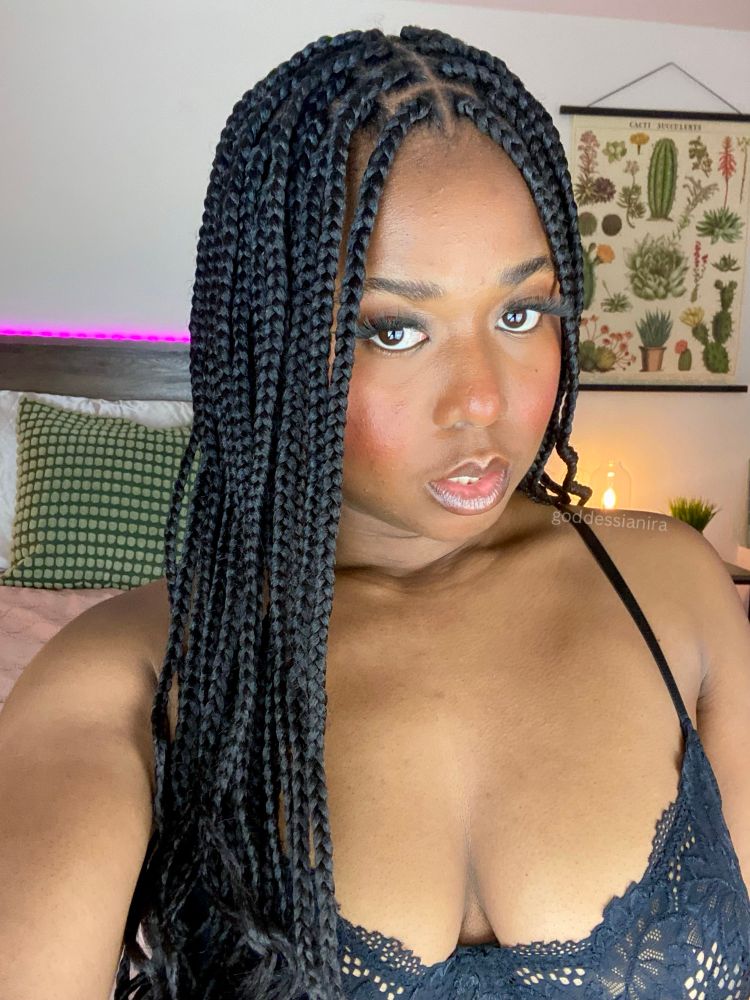 Selfie of Goddess Ianira on Her bed. She gazes at you with a knowing look. She’s aware of Her power. She’s wearing lacy black lingerie. Her skin peeks through slightly. Goddess’ hair is styled in long braids with curls at the ends. She has pretty blush across Her cheeks and nose, Her lips are glossy.