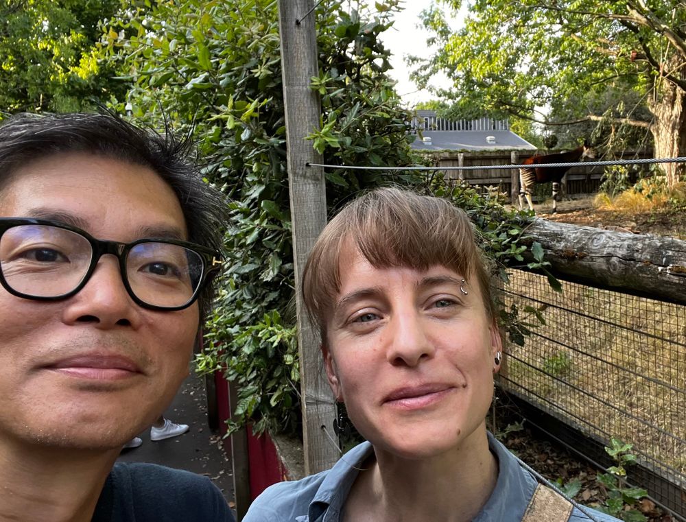 Two people smiling and an okapi in the background 
