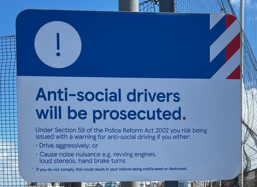 Sign that says:

Anti-social drivers will be prosecuted.
Under Section 59 of the Police Reform Act 2002 you risk being issued with a warning for anti-social driving if you either:
• Drive aggressively; or
• Cause noise nuisance e.g. revving engines, loud stereos, hand brake turns
*if you do not comply, this could result in your vehicle being confiscated or destroyed.