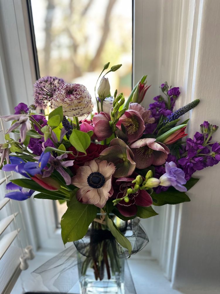 A bouquet of purple flowers in a clear glass vase by the window