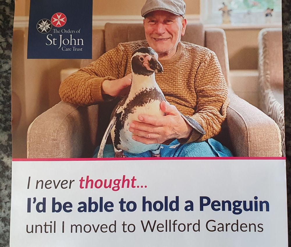A man holding a penguin, with the text "I never thought I'd be able to hold a Penguin until I moved to Wellford Gardens"