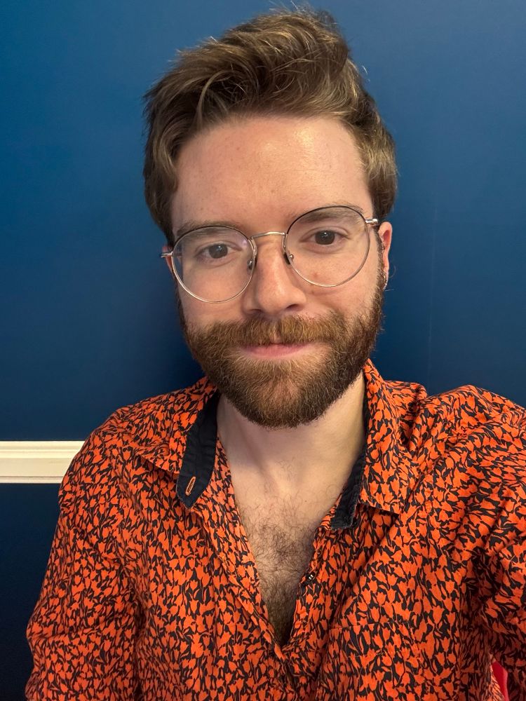 selfie of me wearing an orange tulip print shirt in front of a nicely complimentary blue wall if I do say so myself