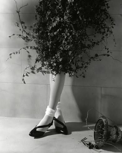 woman in shrubbery leaning against wall with legs cross. take care & see soon