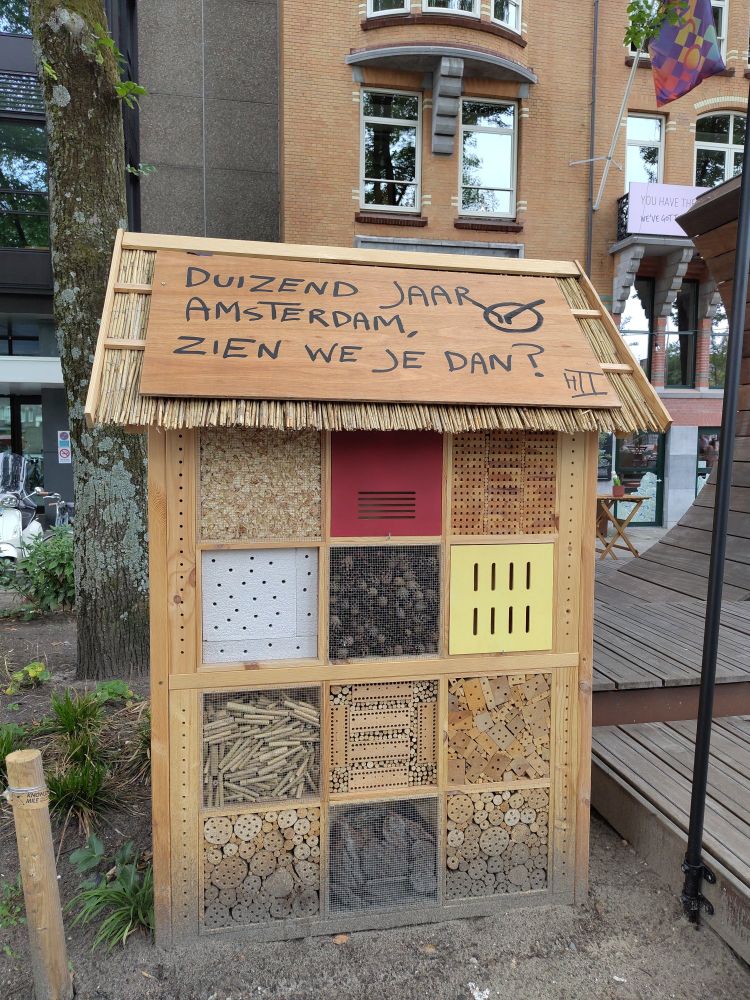 Insect hotel on a busy street in Amsterdam, with text: a thousand years of Amsterdam, will we see you then?