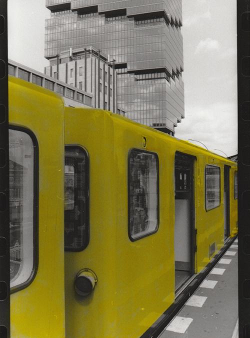Yellow U-bahn cars in front of a tall glass faced building.