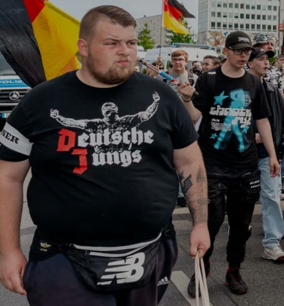 Ein dicker Mann trägt ein T-Shirt mit der Aufschrift "Deutsche Jungs" und einem sportlichen Mann als Bild