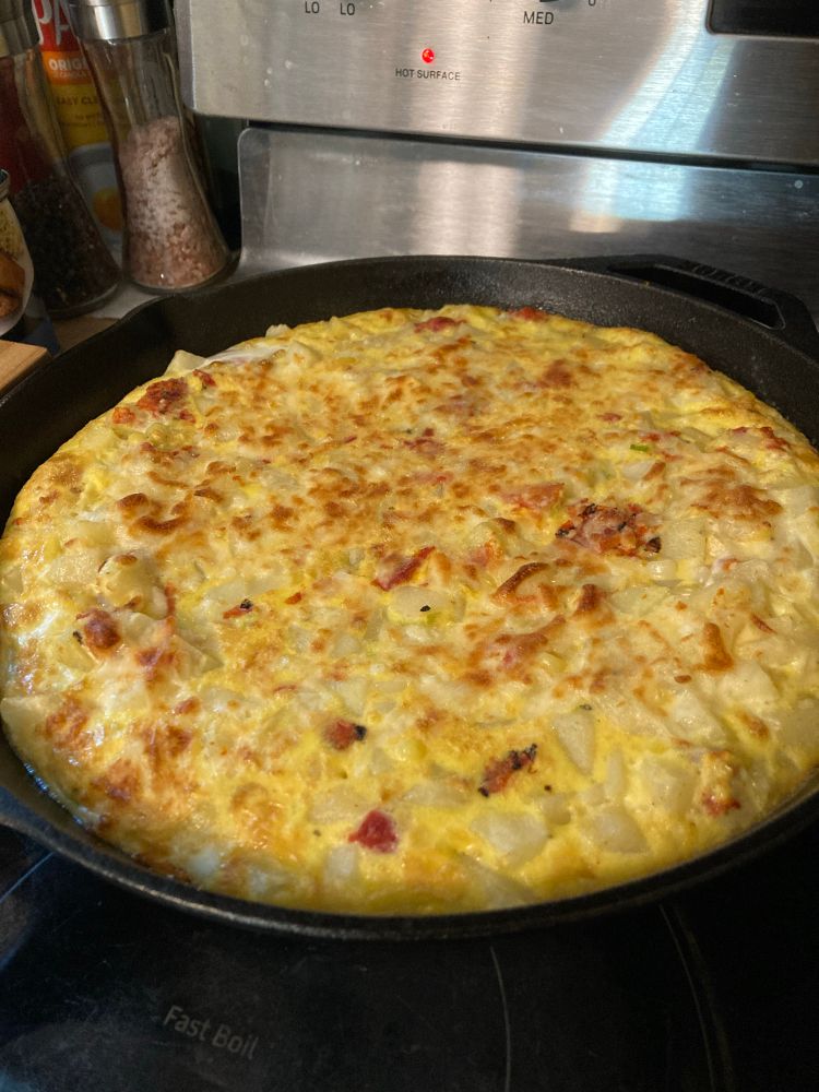 a frittata in a cast iron skillet filled with potatoes, tomatoes, leeks, garlic, cheese, sweet corn