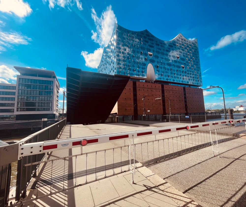 Elbphilharmonie under a bright blue sky. A raised drawbridge in the foreground. 