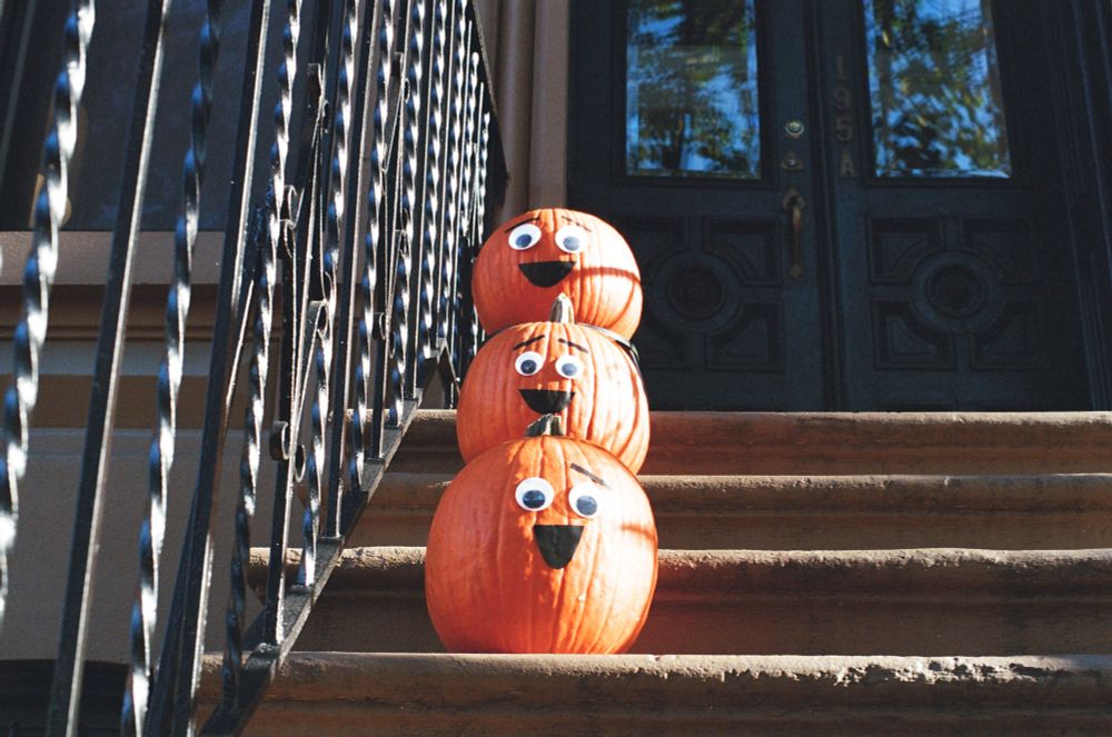 There pumpkins sitting singly lined up on the ascending steps of a brownstone with happy faces drawn on them