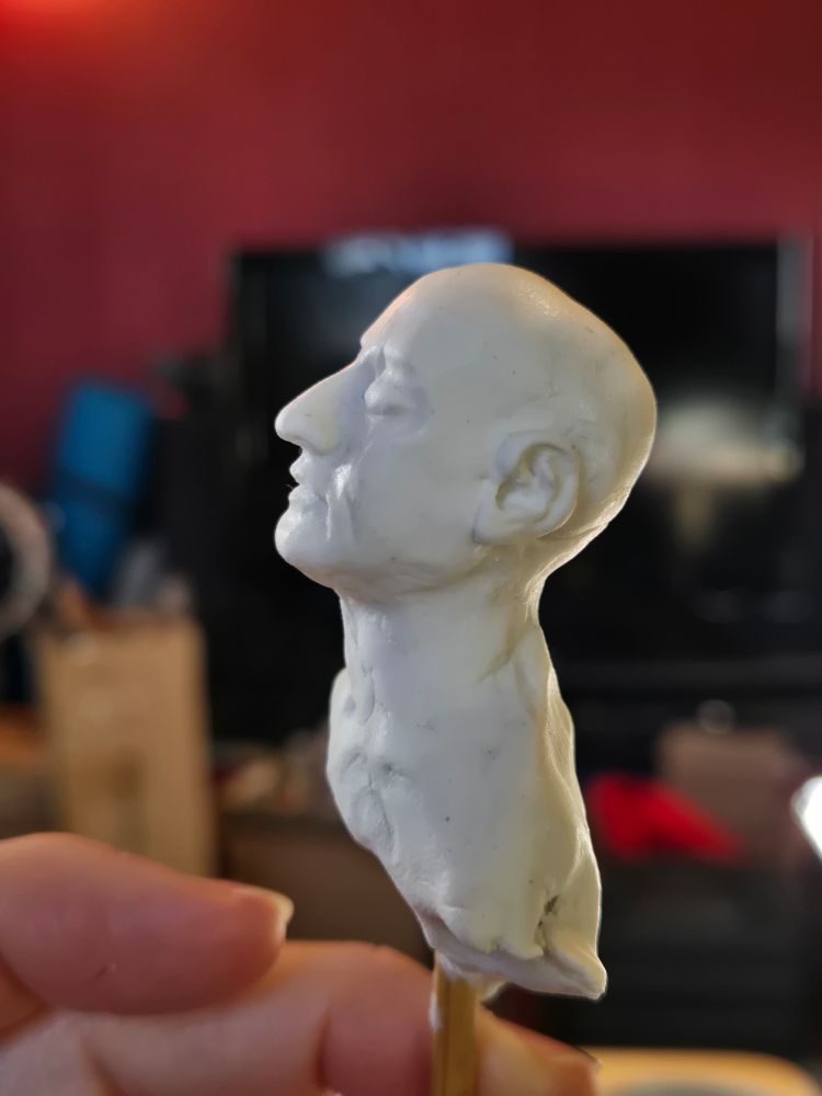 A miniature sculpture of the head and bust of a middle aged woman, in white sculpey clay. Unfinished