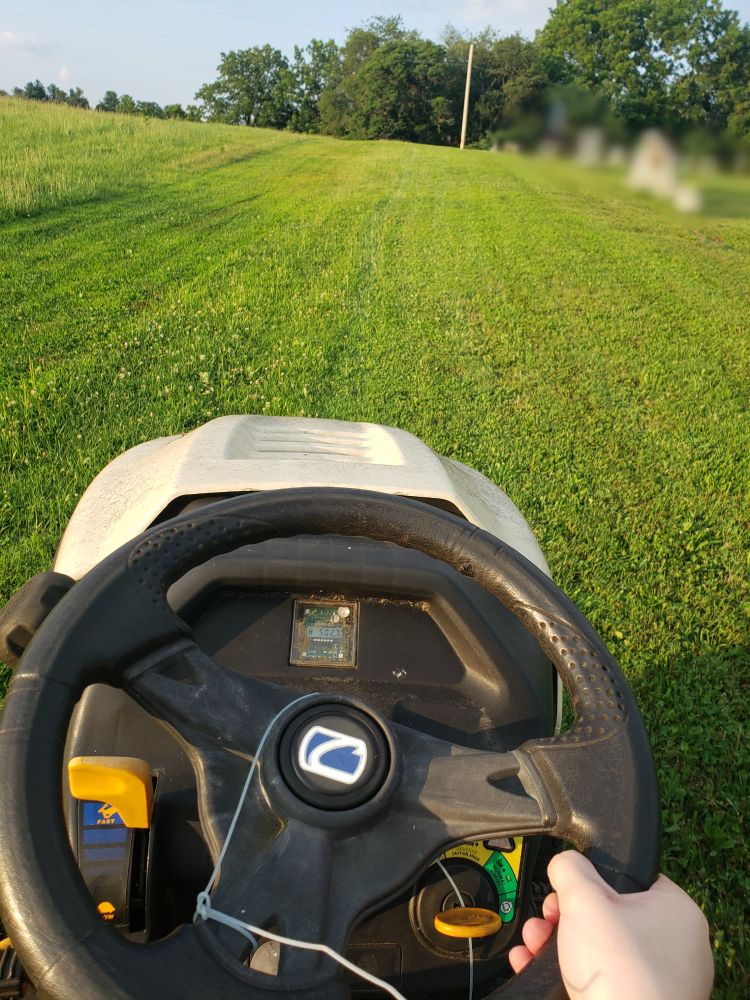 A picture of a tractor mowing grass. I am the one driving it. I made sure to censor the tombstones and my mum for privacy reasons.