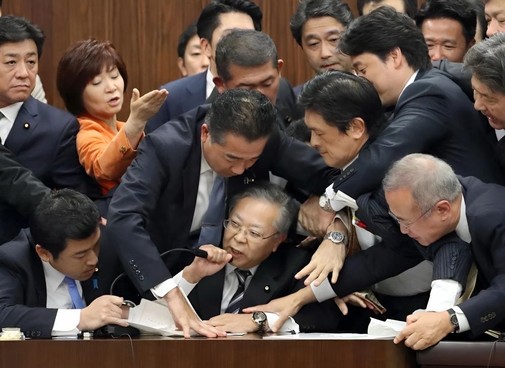 A man at a microphone and many others trying to pull him away