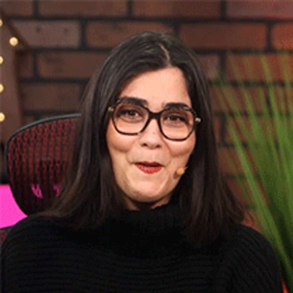 a woman wearing glasses and a black sweater is sitting in a chair with a microphone in her mouth .