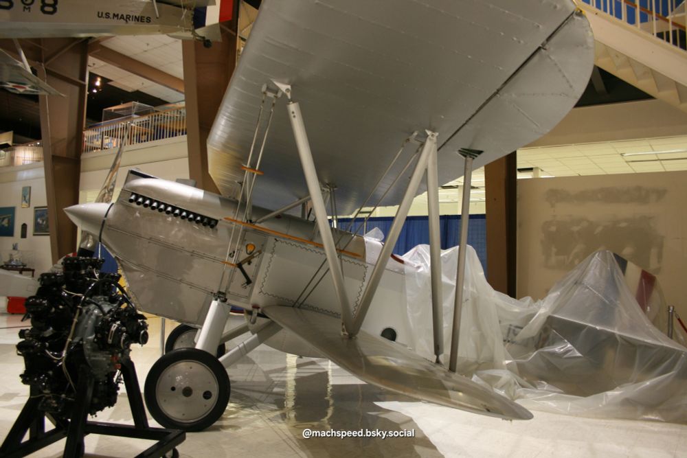 Curtis F6C-1 Hawk biplane in shiny silver. Seen from the left side. Undergoing restoration at the time, the rear of the plane is covered in a clear tarp. A beautiful airplane. Nat. Naval Aviation Museum NAS Pensacola. Photo by @machspeed.bsky.social