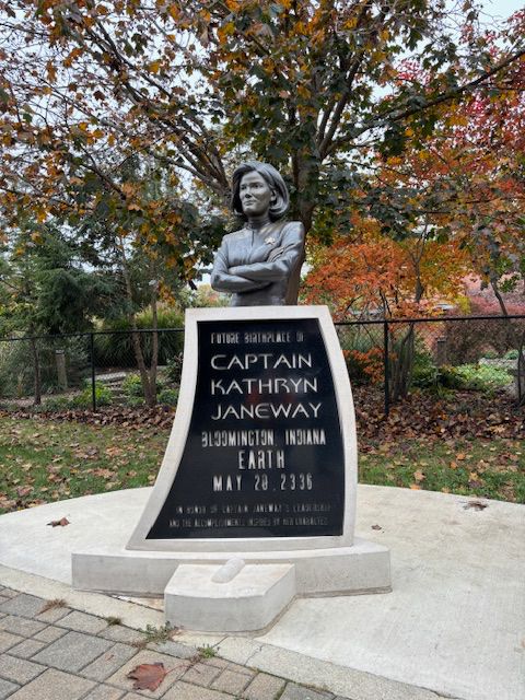 Plaque that says “Future birthplace of Captain Kathryn Janeway, Bloomington Indiana, Earth, May 20, 2336”, with a statue of a woman in uniform crossing her arms above 