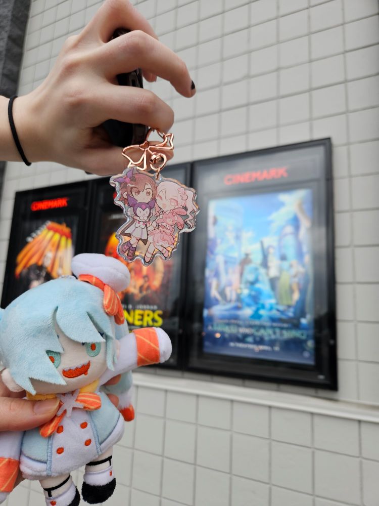 a shrimp sized shrimp miku plushie pointing at the hatsune miku movie poster. also mizuki and ena are there