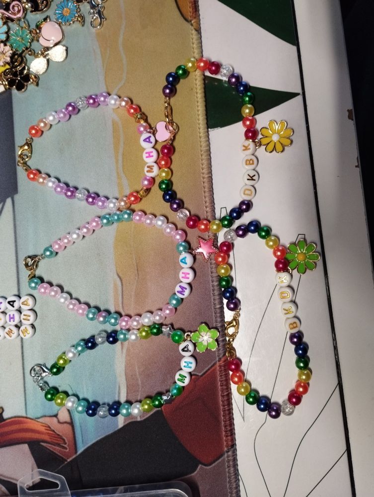 Five colorful bracelets looking like pride flags, three spelling MHA, one spelling BKDK, one spelling DKBK