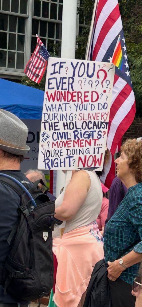 Woman holding sign that reads “ wondered what you do during slavery. The Holocaust were the civil rights movement? You were doing it right now.”