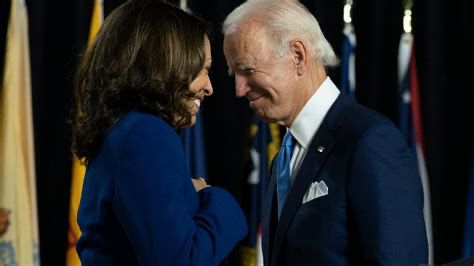 This is a photo of VP Harris (dressed in a blue suit) and President Biden (dressed in a darker blue suit with blue tie, white shirt) facing each other closely and smiling. You can see the mutual respect they have for one another.