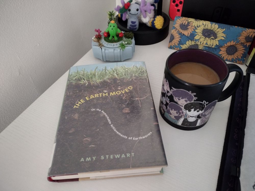 A hardcover book titled The Earth Moved by Amy Stewart. The cover illustrates a world under the green grass within the loose brown soil. 