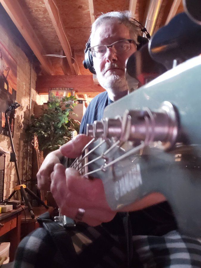 A close up shot of the headstock of my Yamaha BBMA1000. The shot is angled down the neck and you can see my hands and big head. I'm in my BASSment spot and you can see the floor joists.. 