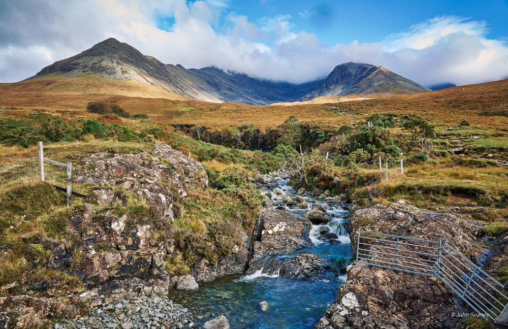The Allt Coire na Banachdich threads its way though rocky banks.  It's flanked by pasture and its golden grass and green shrubbery.  Fences on either side of the small waterfall serve as out-of-bounds markers for the sheep, which we met down on the road.  The sunlit mountains are capped with moving, white clouds that reveal blue skies.  It's not the longest hike that we will do on Skye, but it's the most intimate.  Our Innkeeper recommend a few hikes, all were uncrowded, local gems.  And "of coarse you have to do the Fairy Pools ...like everyone else", as he put it.