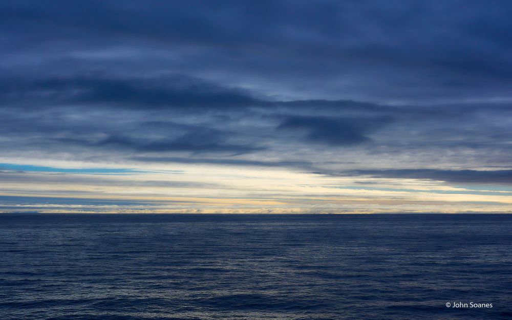 A palette filled with blues, from the dark waters of the Greenland Sea to the dark threatening clouds above.  There's a ribbon of light blue and yellow just above the horizon.  Svalbard and Jan Mayen, Norway