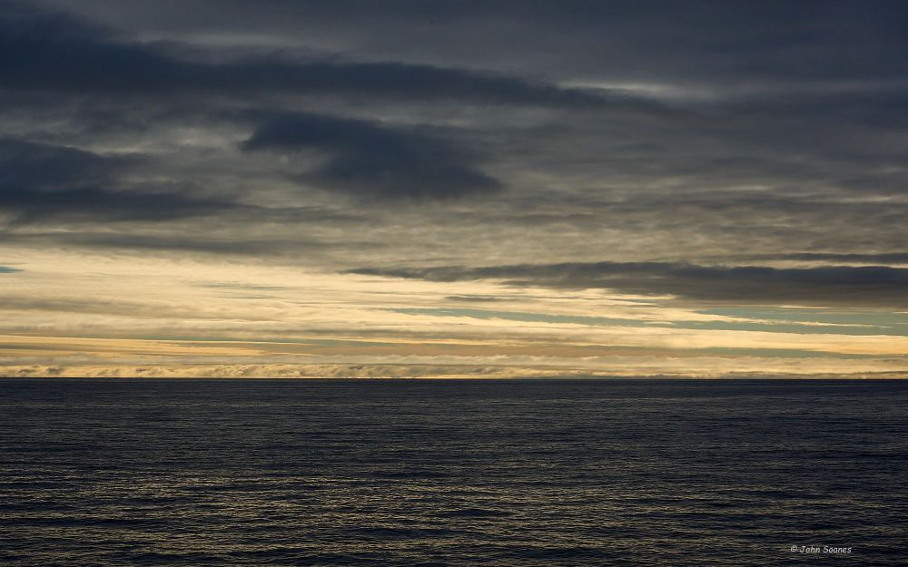 Ribbons of clouds in the late evening sky, in the Artic, near Svalbard.  It was July, so no night sky, the clouds provide the darkness.  Rippled waters of the Greenland Sea fill the bottom third of the image.