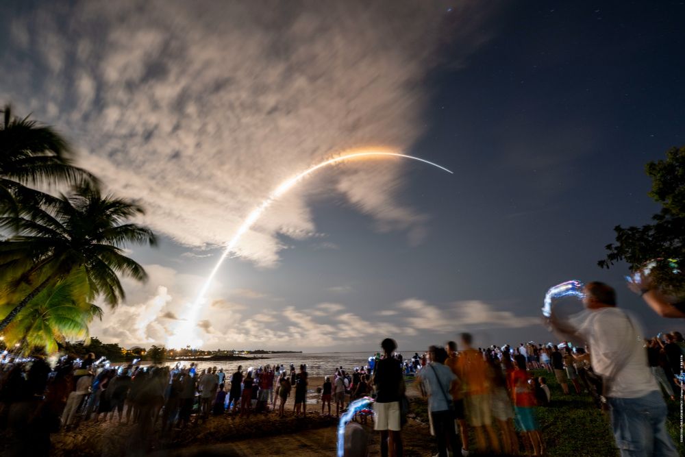 A long-exposure photo of spectators watching the Vega-C VV27 launch from a beach  nearby.
