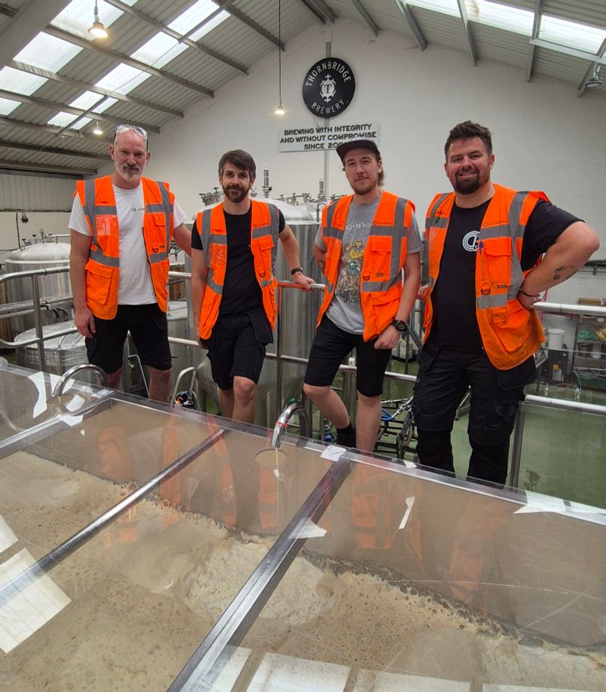 4 chaps from Oakham in Hi-Viz vests, even though I told them they didn't need to wear them, standing in front of the top trough of our Union system, full of fermenting frothy wort.