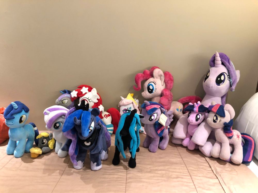 Photograph of multiple My Little Pony plush toys on a bed, including officially released and custom made ones. 
