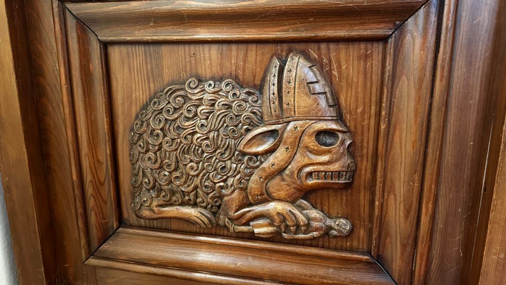 Die Seite einer Bank auf der ein Monster/Raubtier mit Bischofsmütze abgebildet ist.