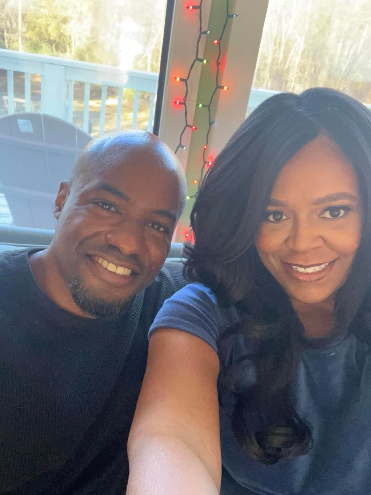 Two people (male on the left - Kevin & female on the right - actress, Kerry) smiling and taking a selfie. Christmas lights are hanging in the background. 