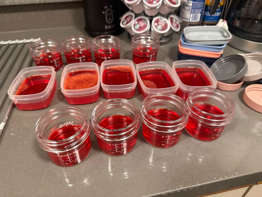 Three rows of raspberry jello in containers in a countertop.