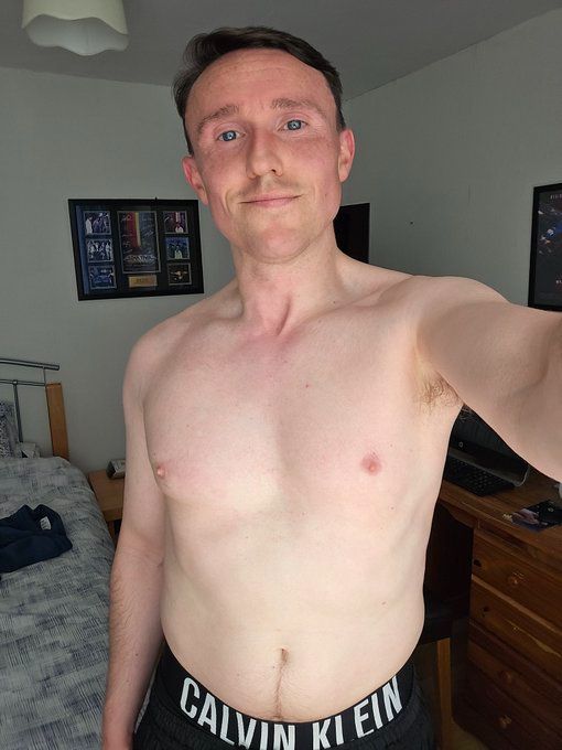 David is standing shirtless in his bedroom wearing shorts and Calvin Klein underwear smiling slightly at the camera 