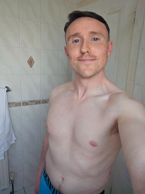 David is in his bathroom standing shirtless in Calvin Klein underwear holding his phone and smiling slightly at the camera 