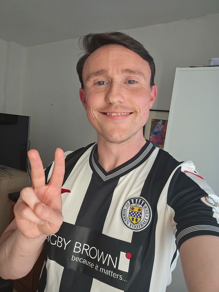 David is in his bedroom wearing a St Mirren football home strip smiling at the camera and making a peace sign