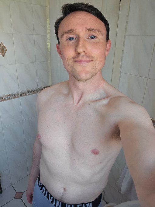 David is in his bathroom shirtless in Calvin Klein underwear smiling slightly at the camera