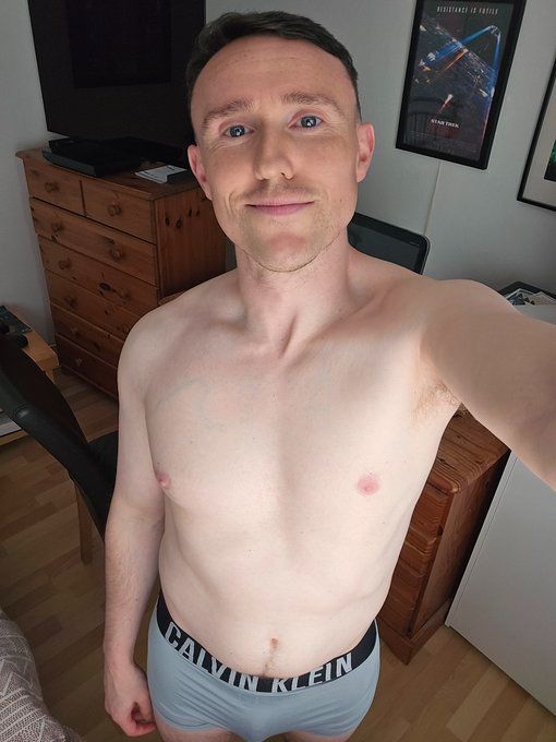 David is standing shirtless in his bedroom in Calvin Klein underwear looking up at the camera with a slight smile 
