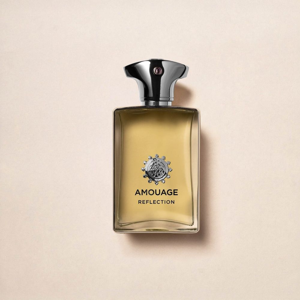 A photo of a jar of cologne labeled "Amouage Reflection." Its a clear liquid in the container but appears gold while viewing the off white background through it.