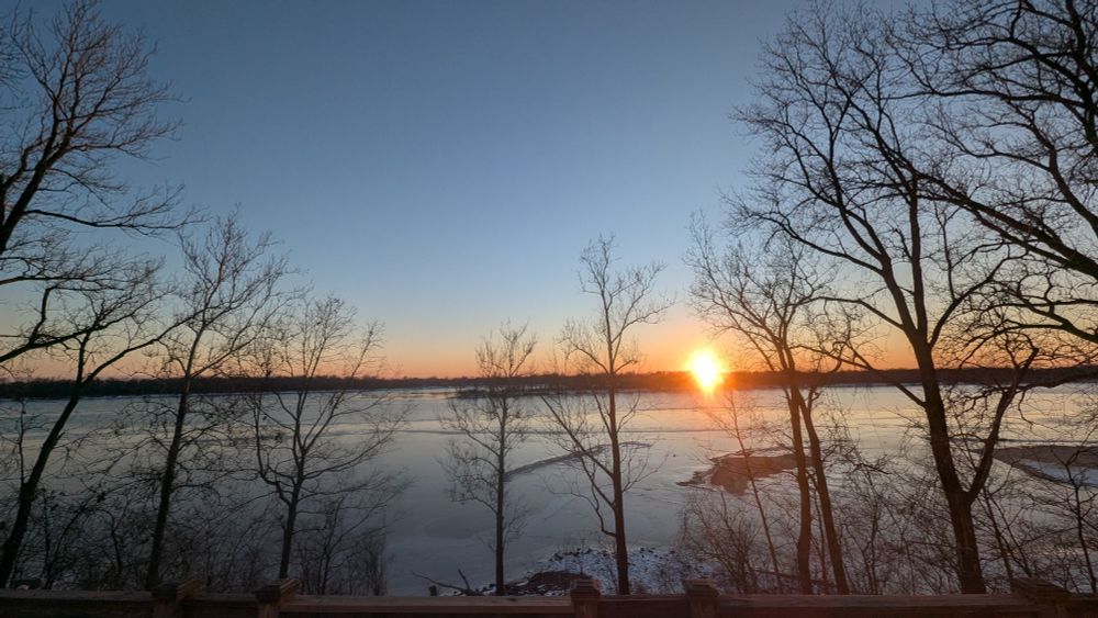 Sunset over the Mississippi River 1/14/25. Shows the sun just disappearing through the leafless trees on the far shore. 